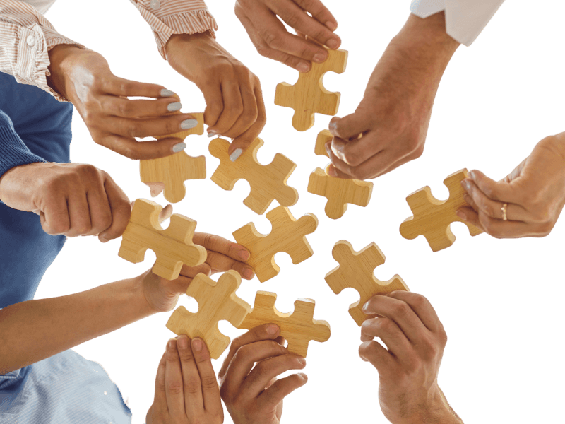 Συνεργασία ομάδας με πολλά χέρια που συνδέουν κομμάτια παζλ – σύμβολο ομαδικότητας και συνεργασίας στη Solid Skills.
